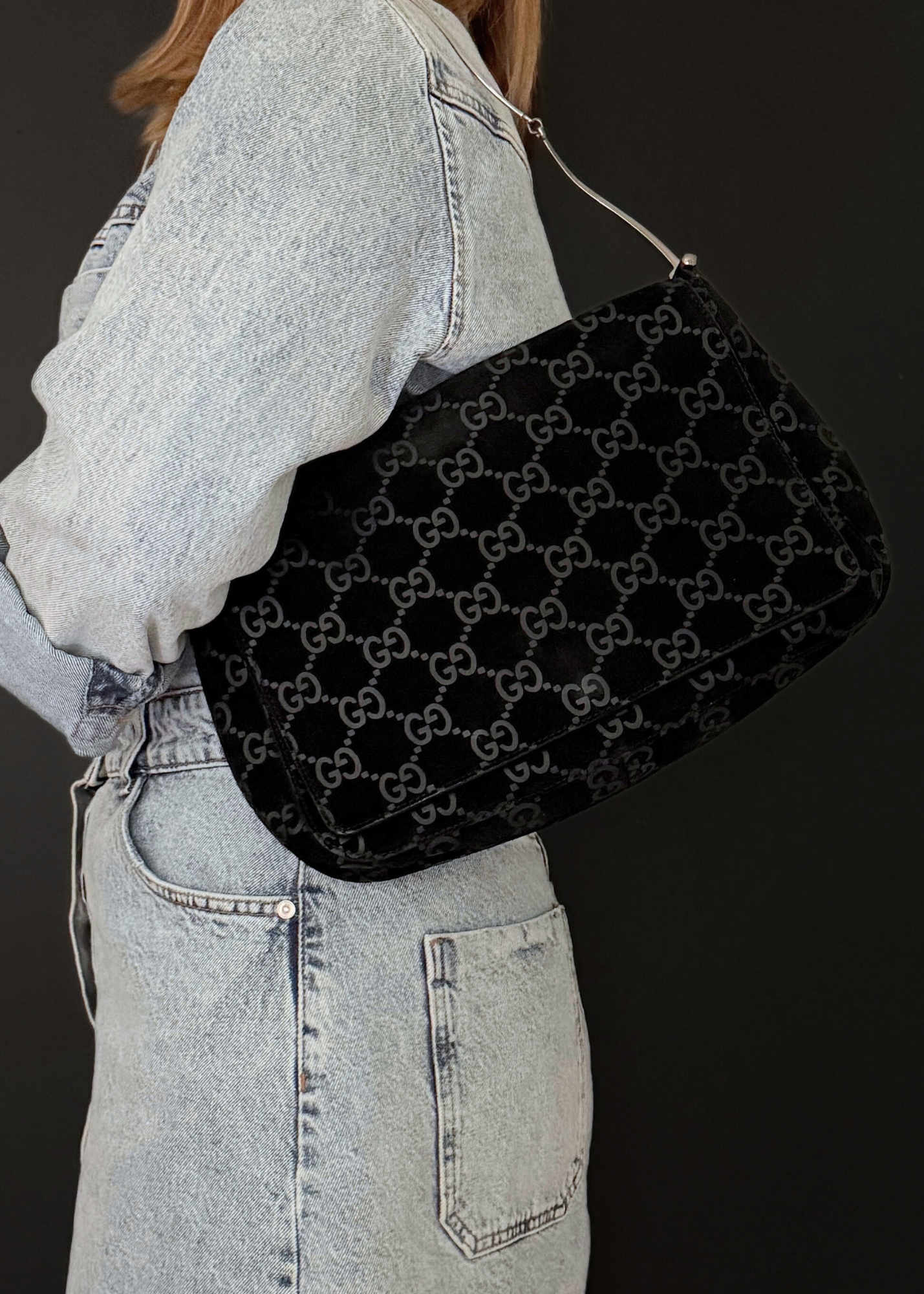 Person wearing a black vintage Gucci bag over one shoulder against a dark background