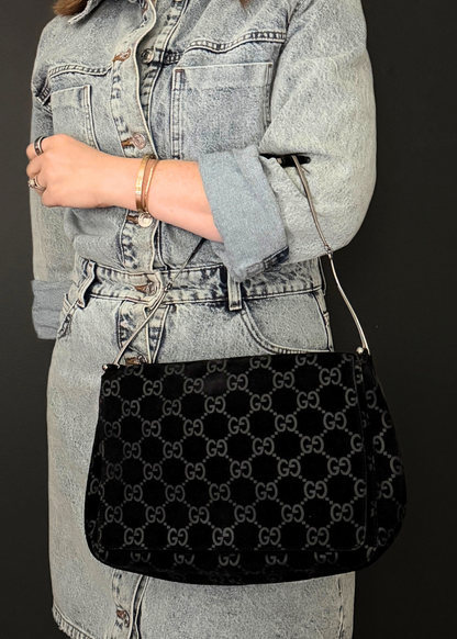 Person wearing a black vintage patterned Gucci handbag with a denim jacket and skirt.