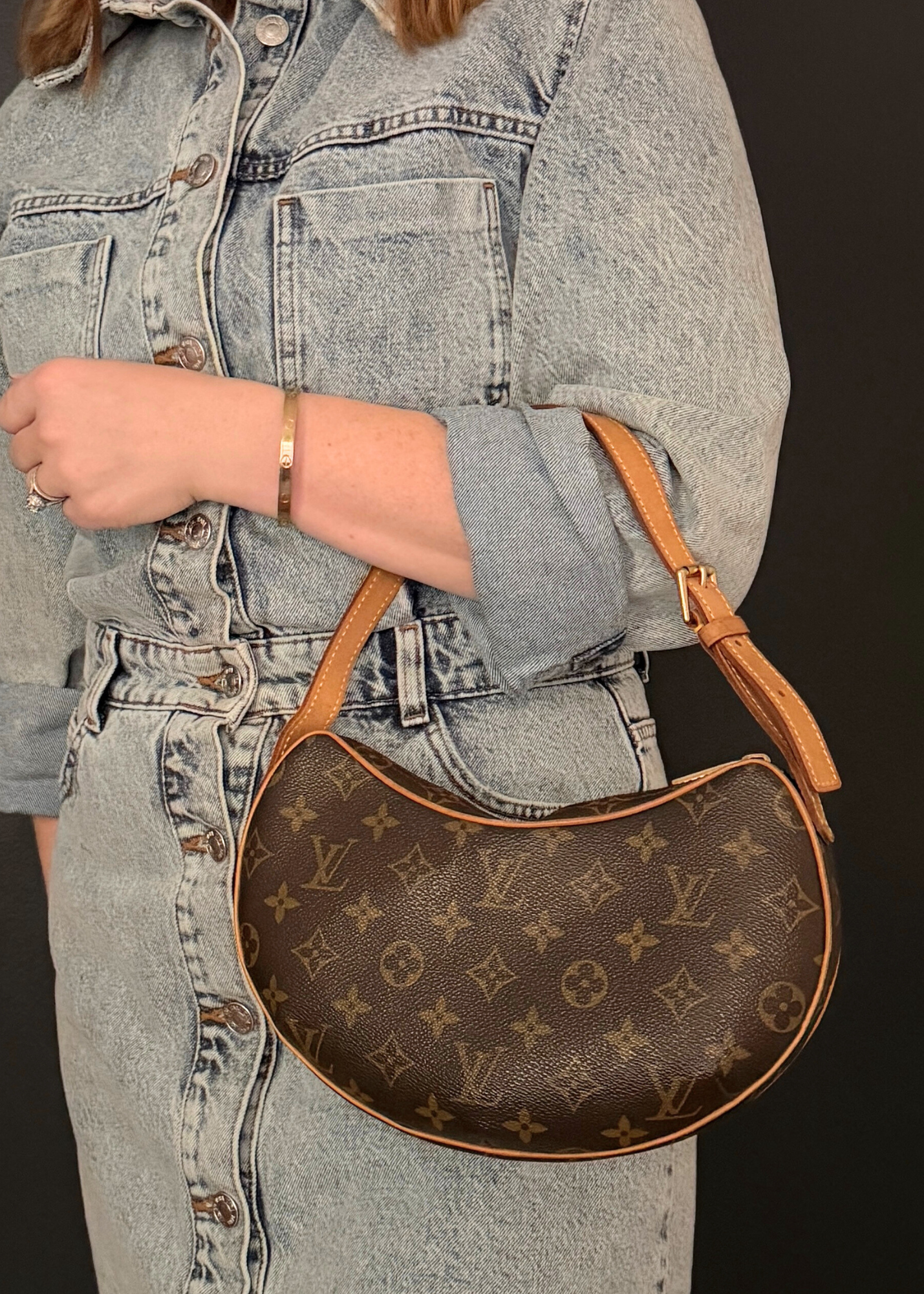 Person wearing a denim jacket and jeans holding a vintage Louis Vuitton brown handbag with a distinctive pattern.