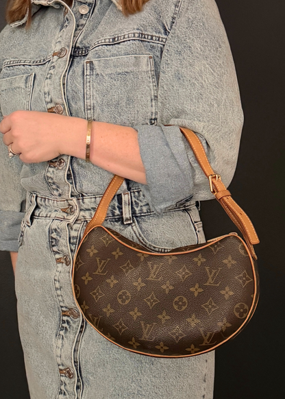 Person wearing a denim jacket and jeans holding a vintage Louis Vuitton brown handbag with a distinctive pattern.