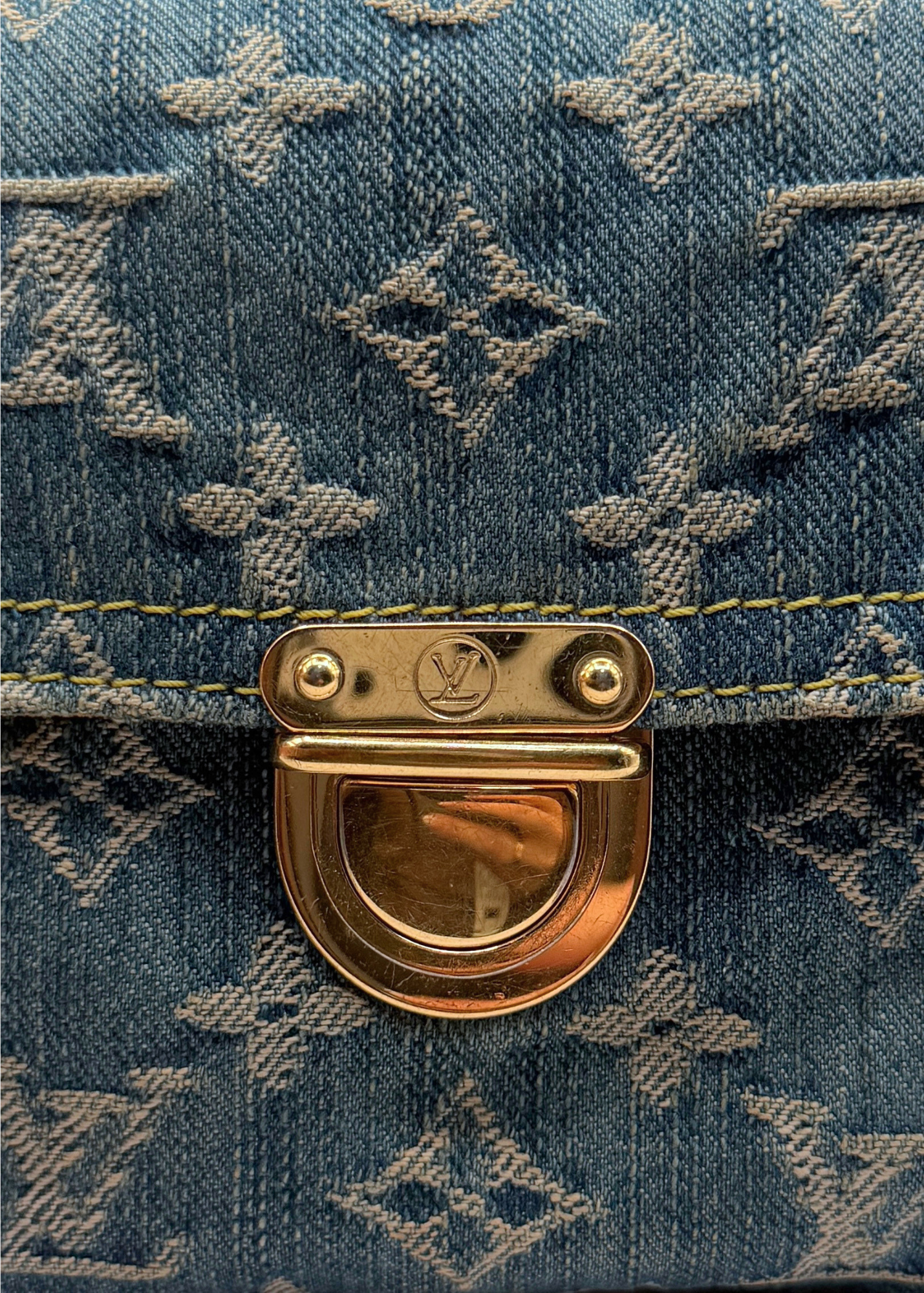 Close-up of a blue vintage Louis Vuitton denim pochette bag with gold hardware featuring a brand logo.