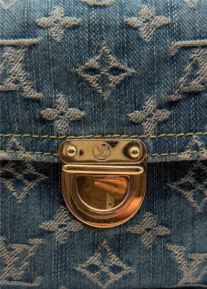 Close-up of a blue vintage Louis Vuitton denim pochette bag with gold hardware featuring a brand logo.