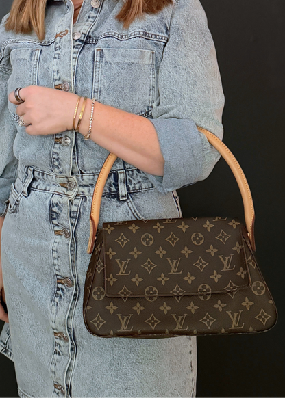 Person holding a brown vintage Louis Vuitton handbag with a pattern, wearing a denim jacket.