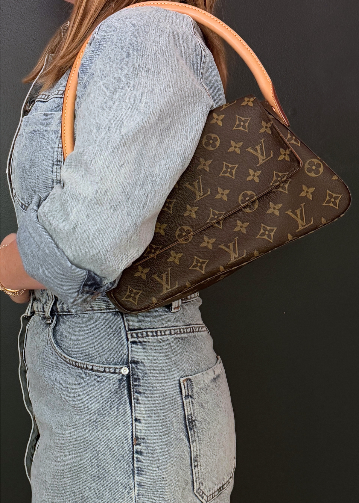 Person wearing a brown Louis Vuitton handbag with a monogram pattern on a dark background