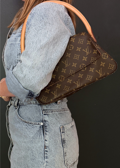 Person wearing a brown Louis Vuitton handbag with a monogram pattern on a dark background