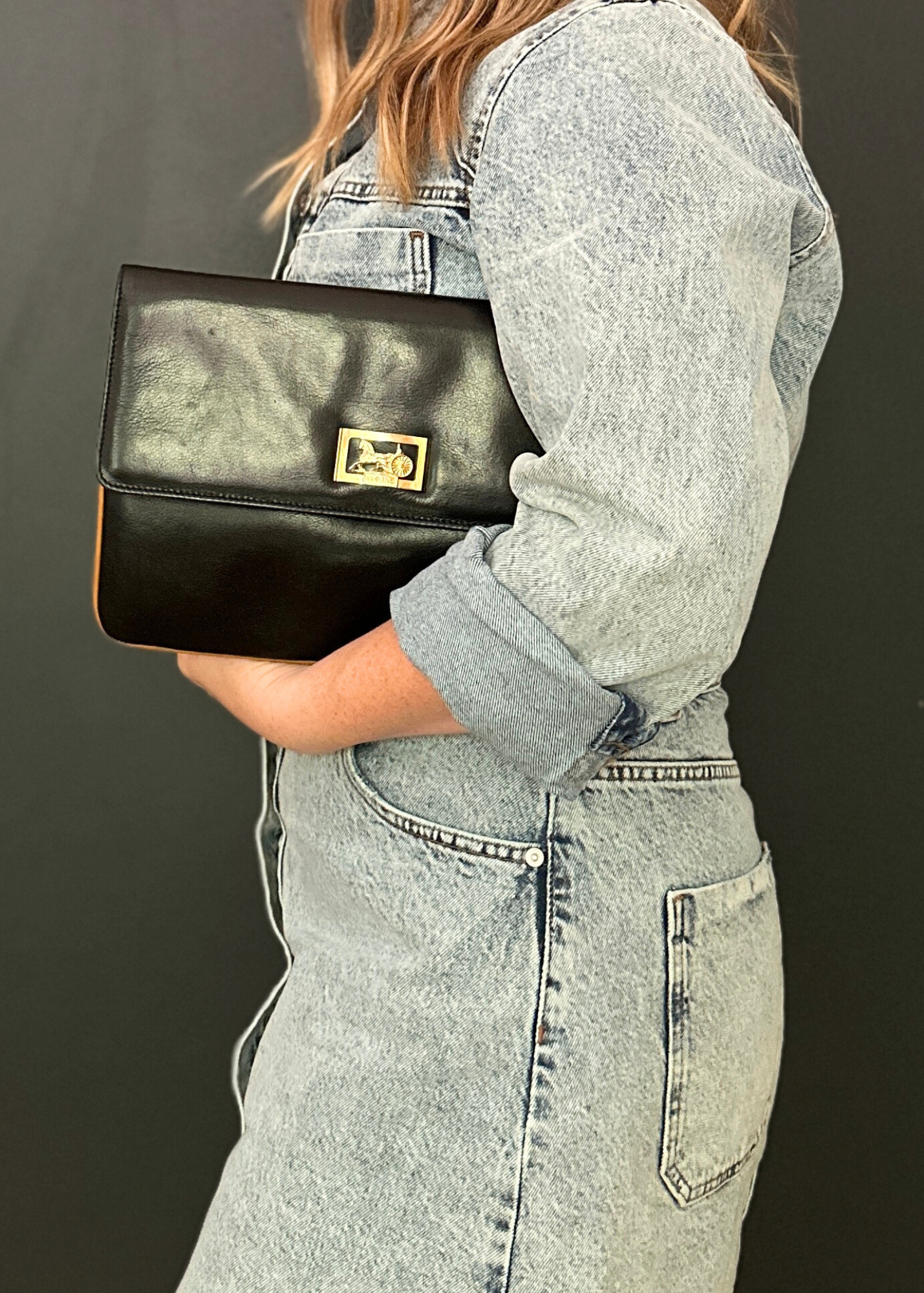 Person holding a black Celine clutch with a gold clasp against a dark background