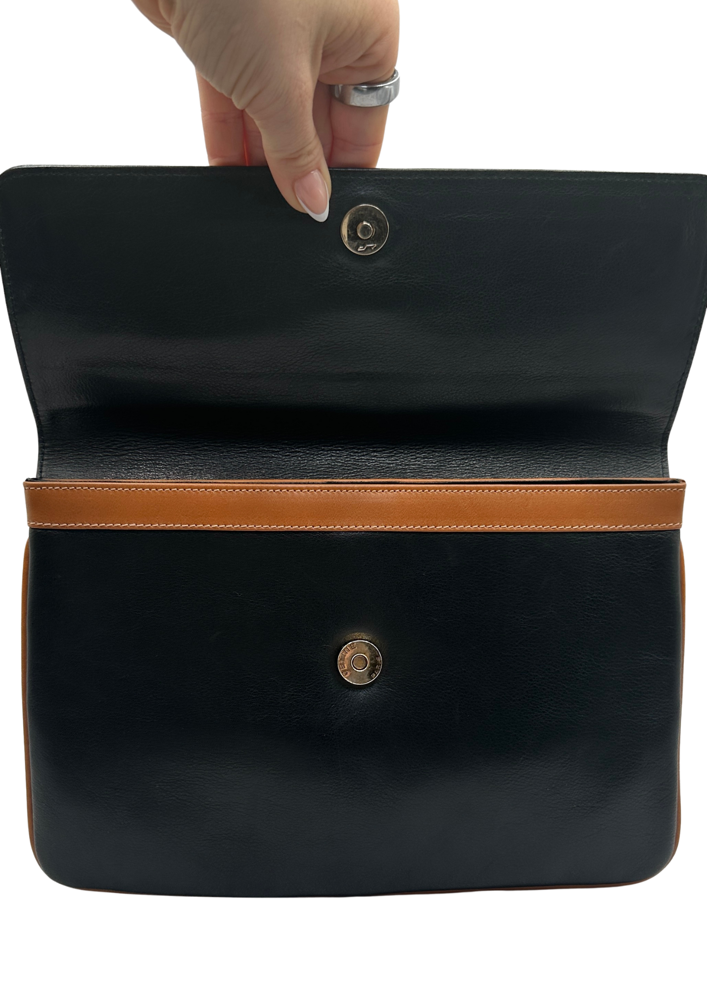 Black leather Celine clutch bag with brown trim held by a hand on a white background