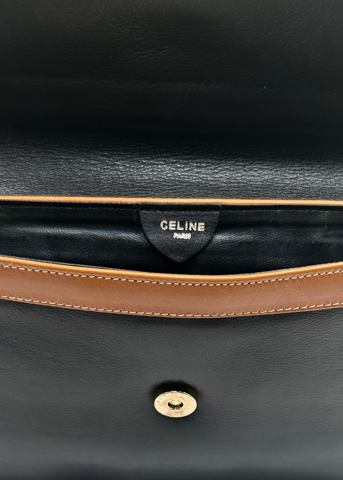 Close-up of a black leather bag with brown trim and Celine logo.