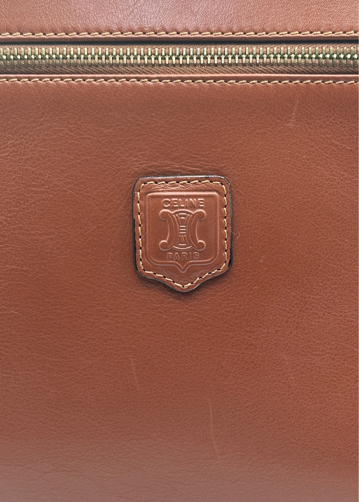 Close-up of a brown leather bag with a brand logo on a matching brown background