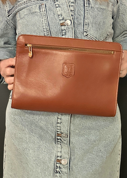Brown leather clutch held by a person wearing a denim dress