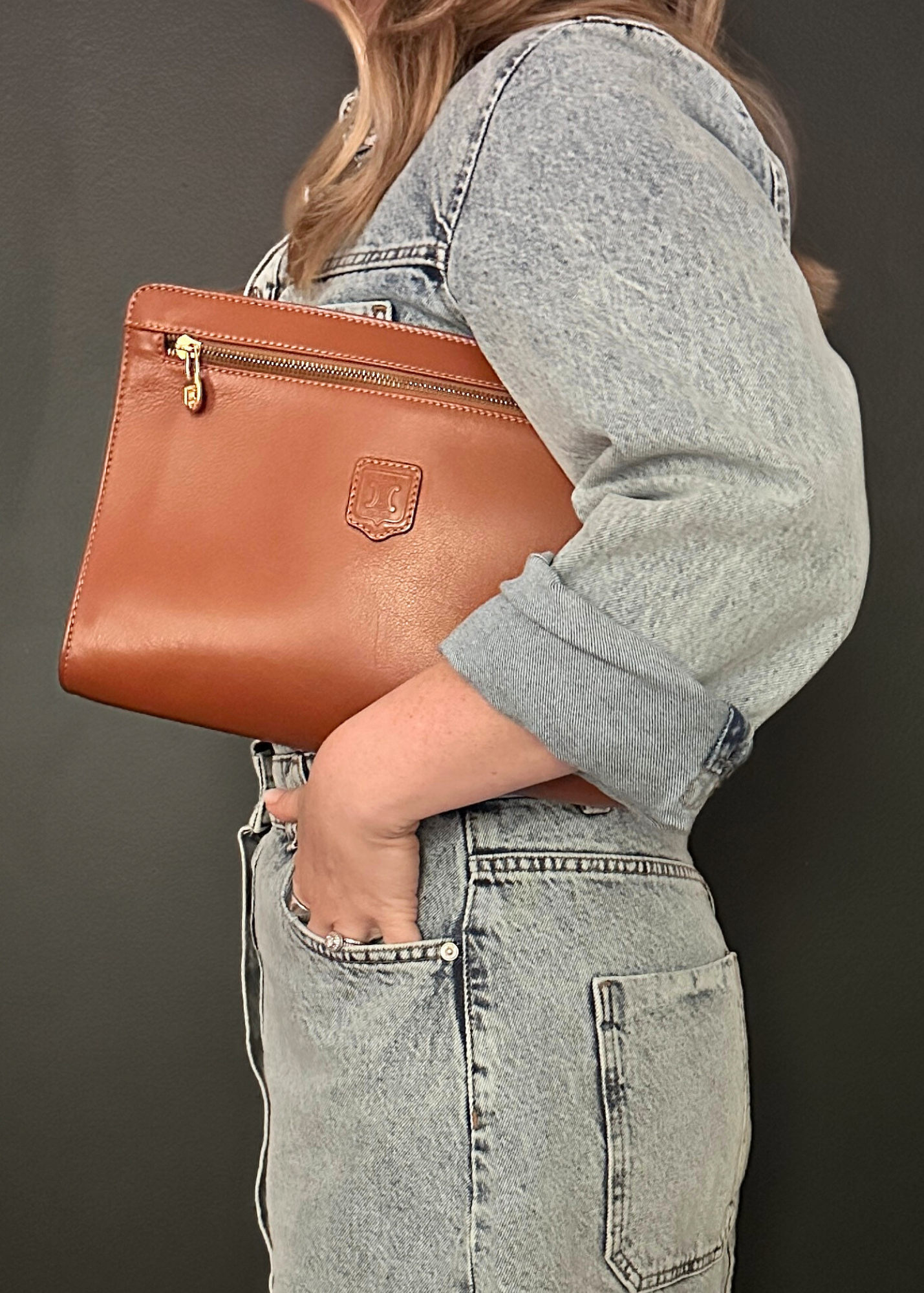 Person holding a brown leather clutch bag against a dark background