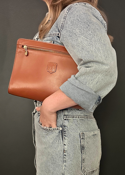Person holding a brown leather clutch bag against a dark background