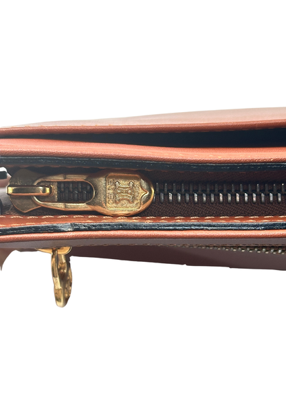 Close-up of a brown leather handbag with gold zipper and clasp on a white background
