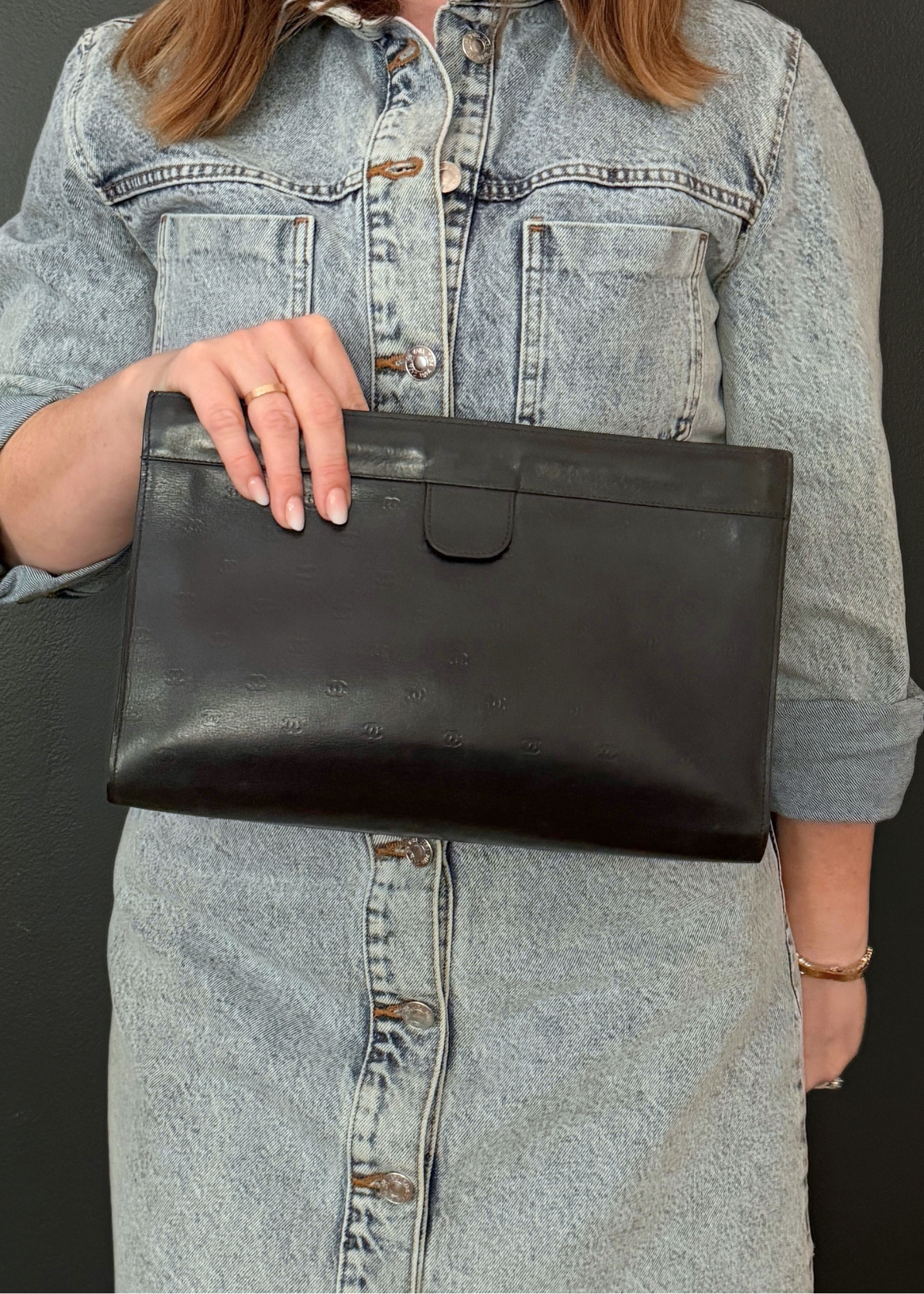 Person holding a vintage Chanel black leather clutch bag with a denim jacket