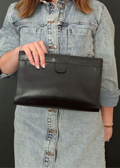 Person holding a vintage Chanel black leather clutch bag with a denim jacket
