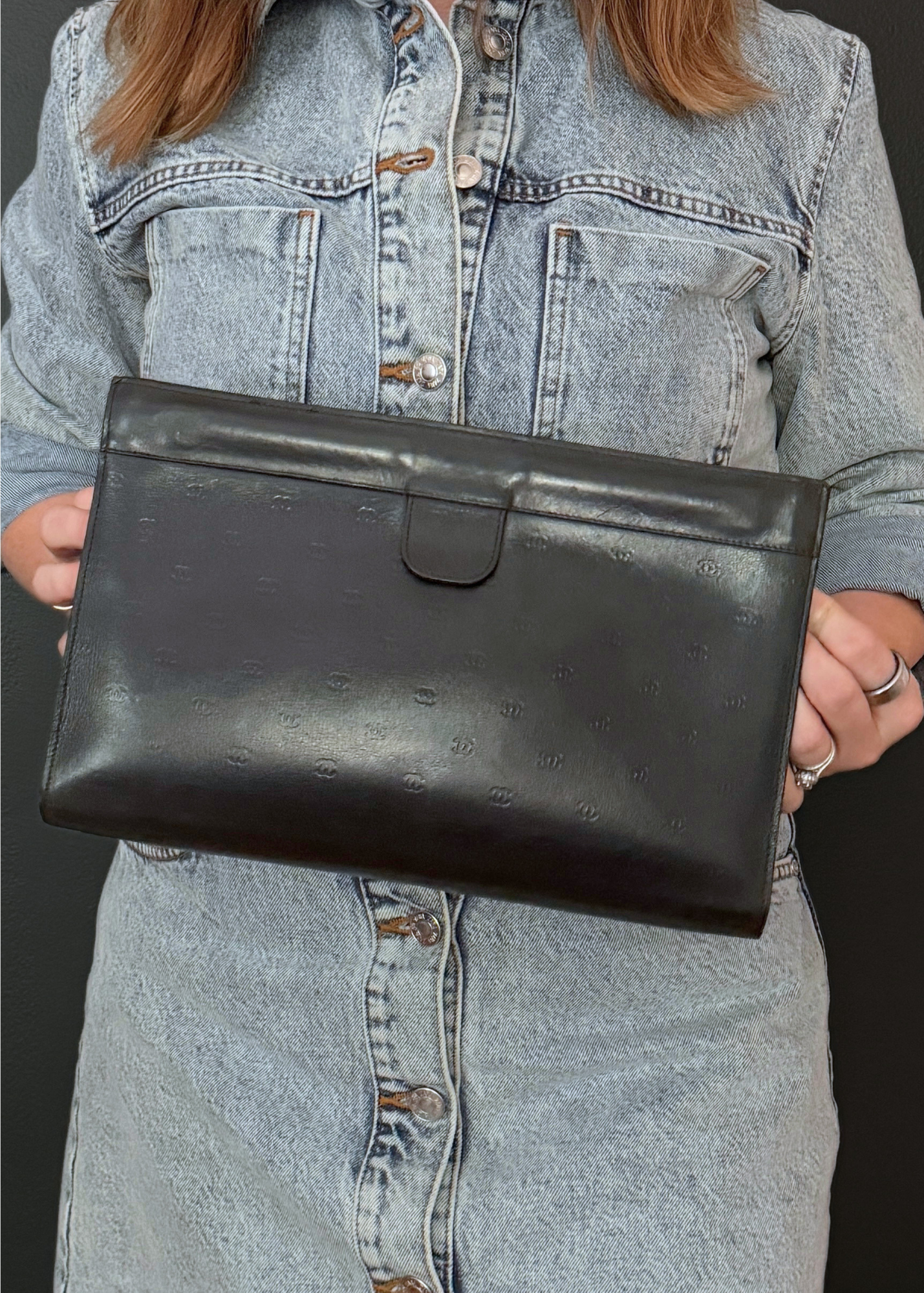 Person holding a vintage Chanel black leather clutch against a denim background