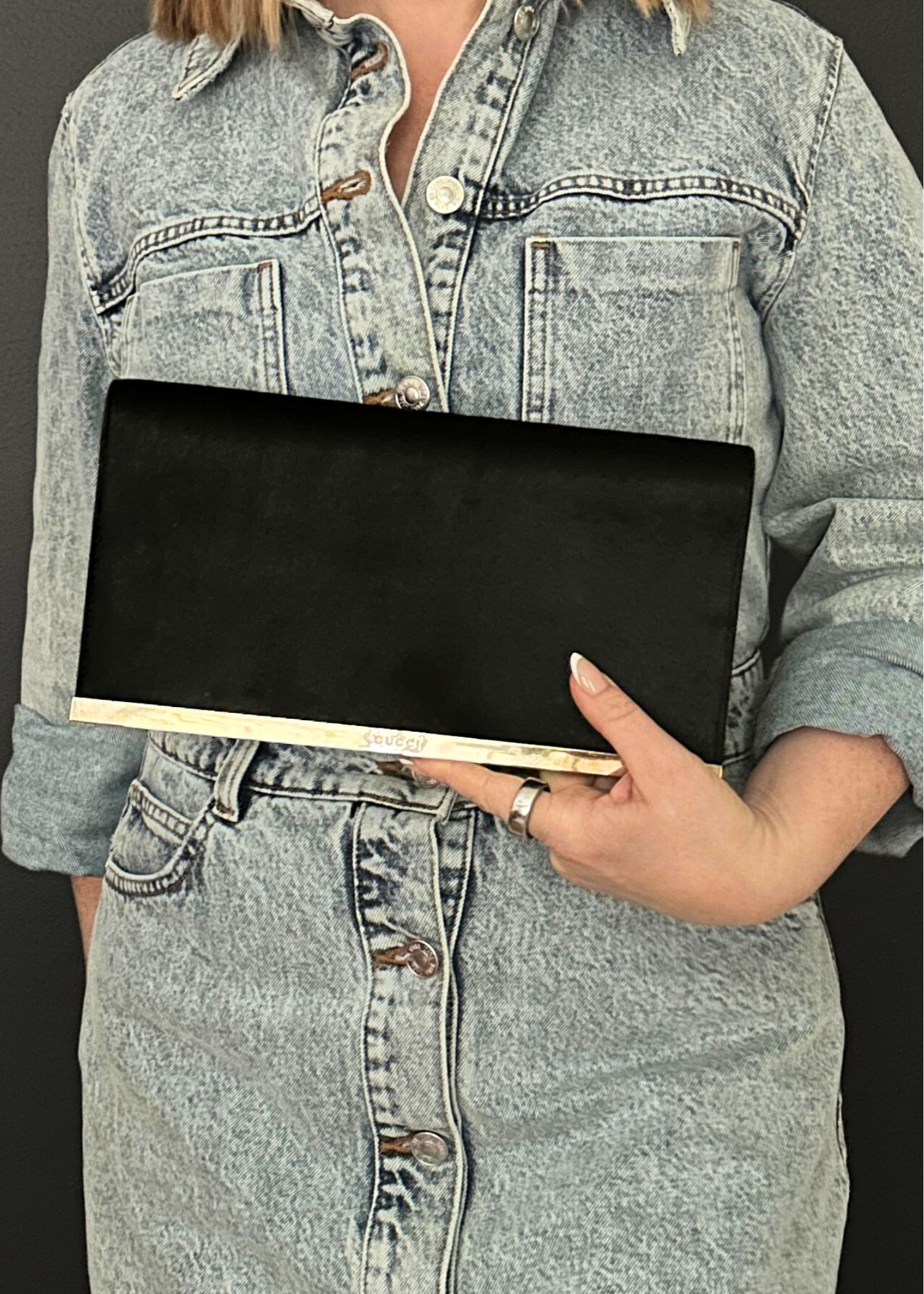 Person wearing a denim jacket holding a black vintage Gucci clutch bag.