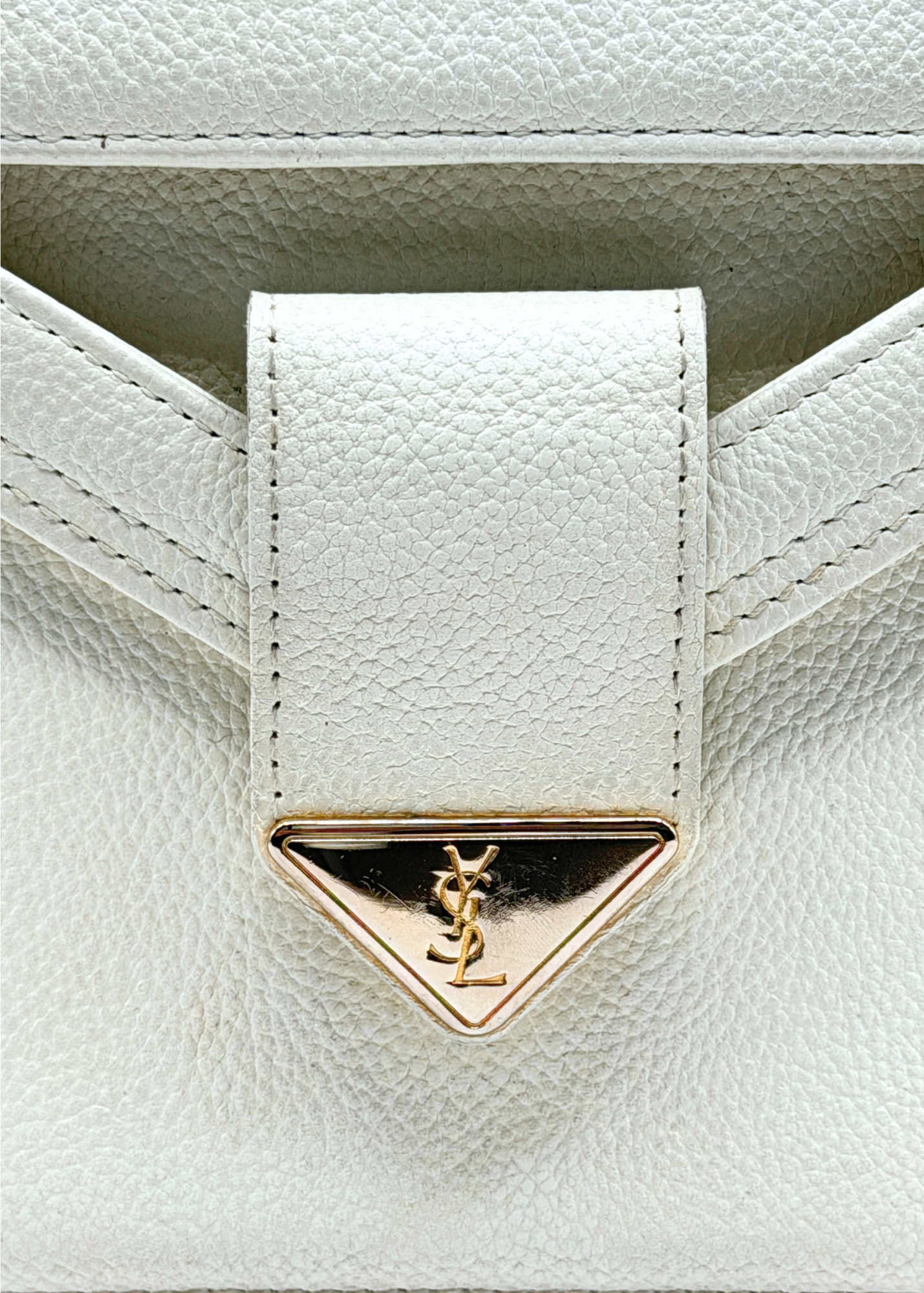 Close-up of a white leather handbag with a gold triangle emblem featuring a Yves Saint Laurent YSL logo.