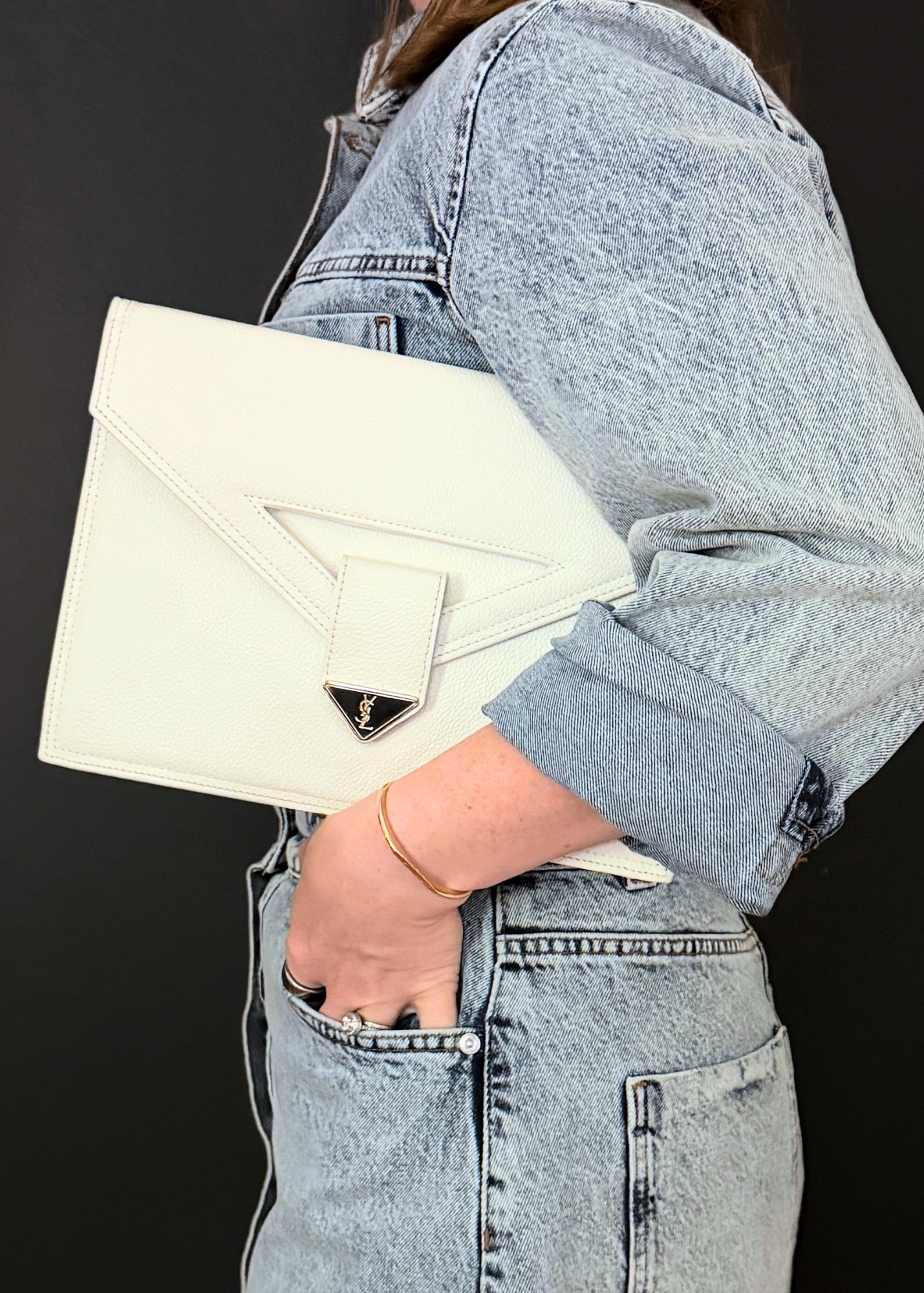 Person holding a cream-colored vintage Yves Saint Laurent clutch with a brand logo against a black background