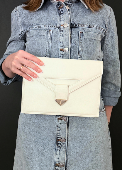 Person holding a cream-colored vintage Yves Saint Laurent clutch bag against a black background