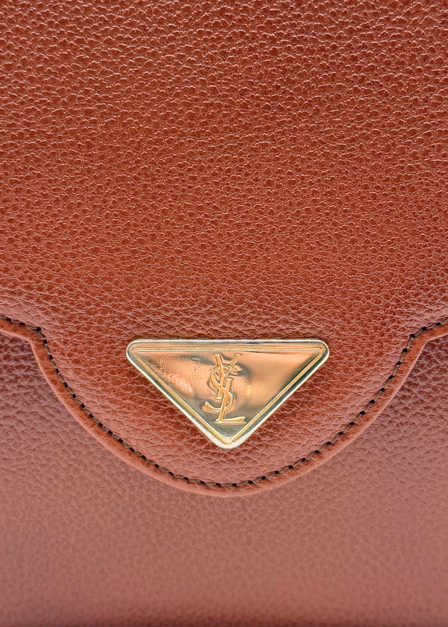 Close-up of a vintage YSL brown leather bag with a gold logo emblem.