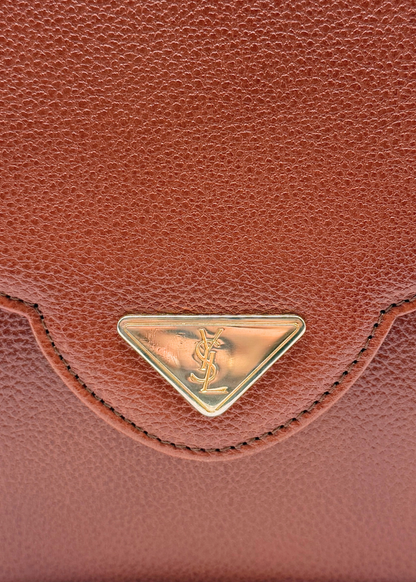 Close-up of a vintage YSL brown leather bag with a gold logo emblem.