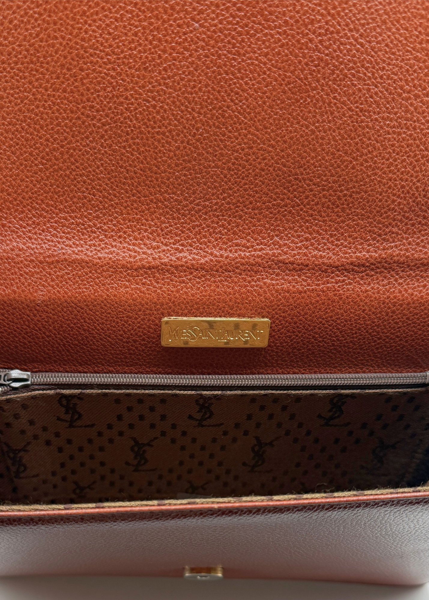 Brown vintage pebbled leather YSL clutch with a gold tag and patterned interior on a white background