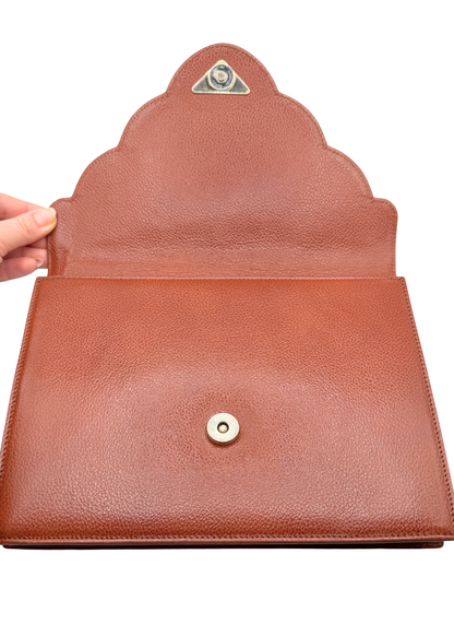Brown vintage pebbled leather YSL clutch bag with a hand holding it open on a white background