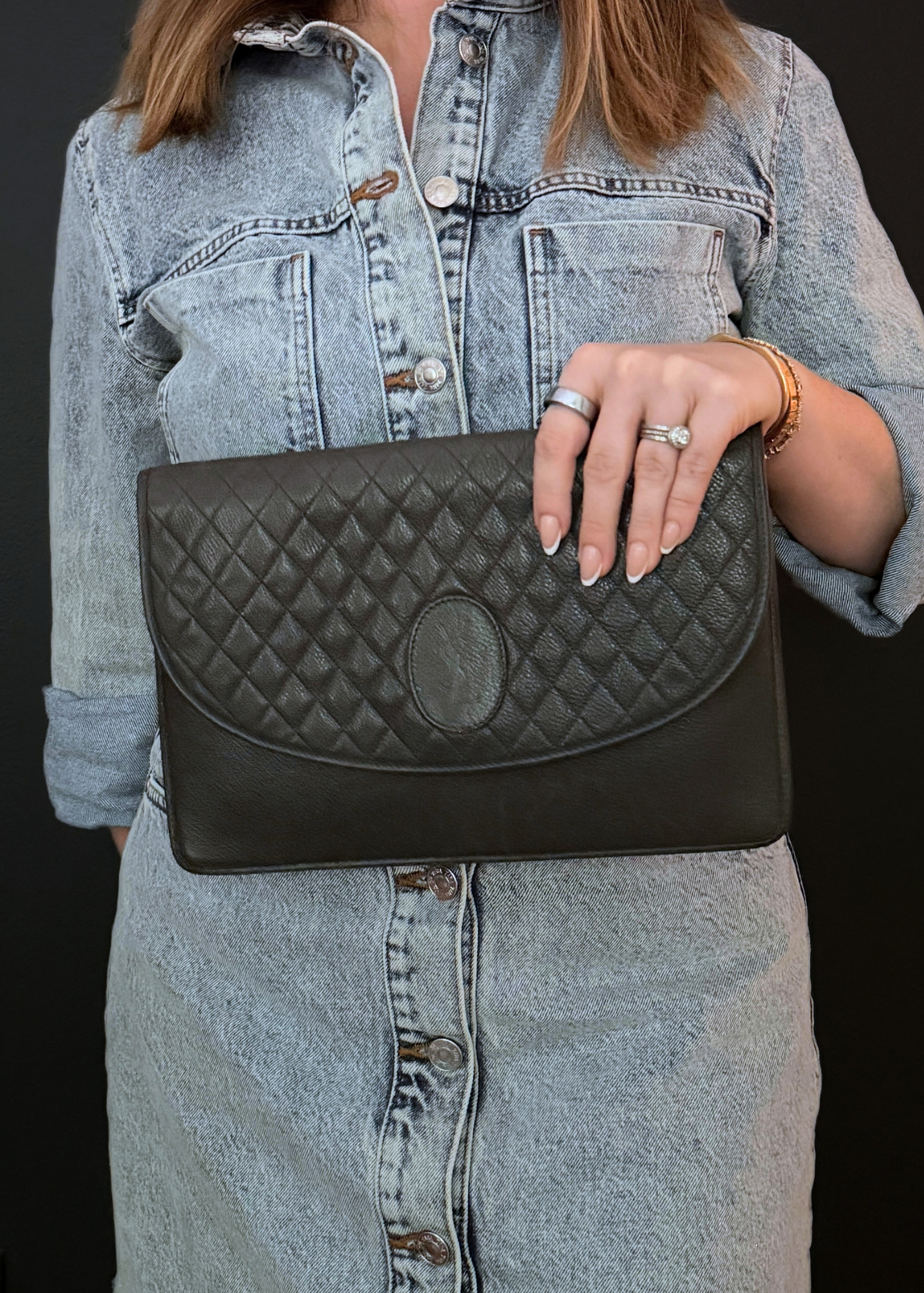 Person holding a taupe vintage YSL quilted clutch bag against a dark background