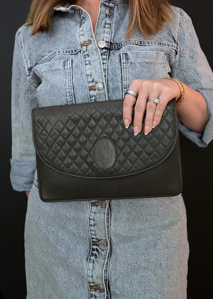 Person holding a taupe vintage YSL quilted clutch bag against a dark background