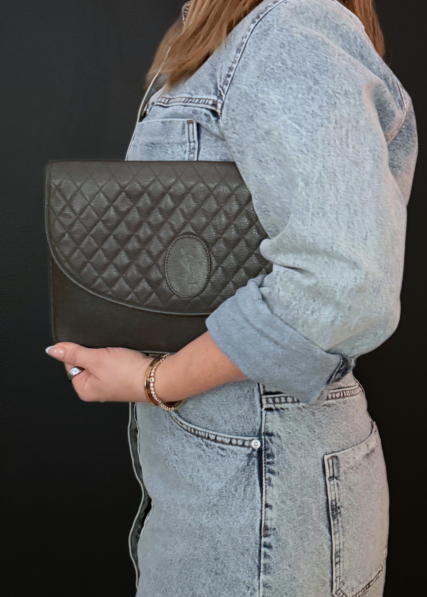 Person holding a vintage YSL quilted clutch bag against a black background