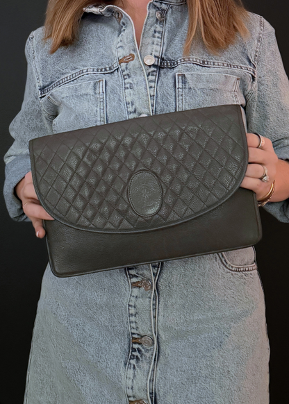 Person holding a quilted taupe vintage YSL clutch bag against a dark background
