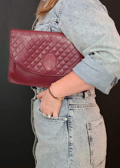 Person holding a vintage burgundy red quilted handbag with a visible YSL brand logo against a dark background