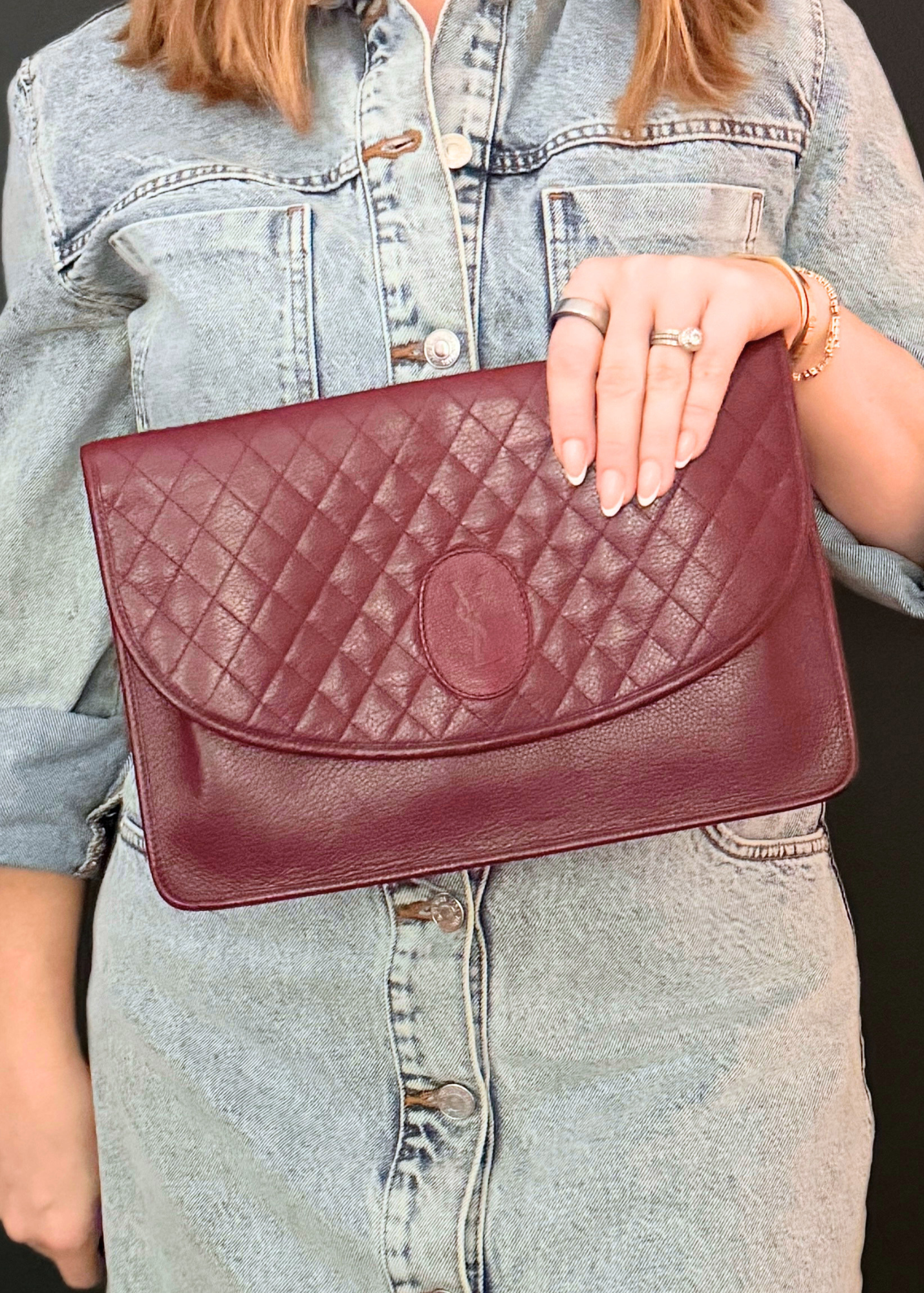 Person holding a burgundy vintage quilted YSL clutch bag with denim jacket