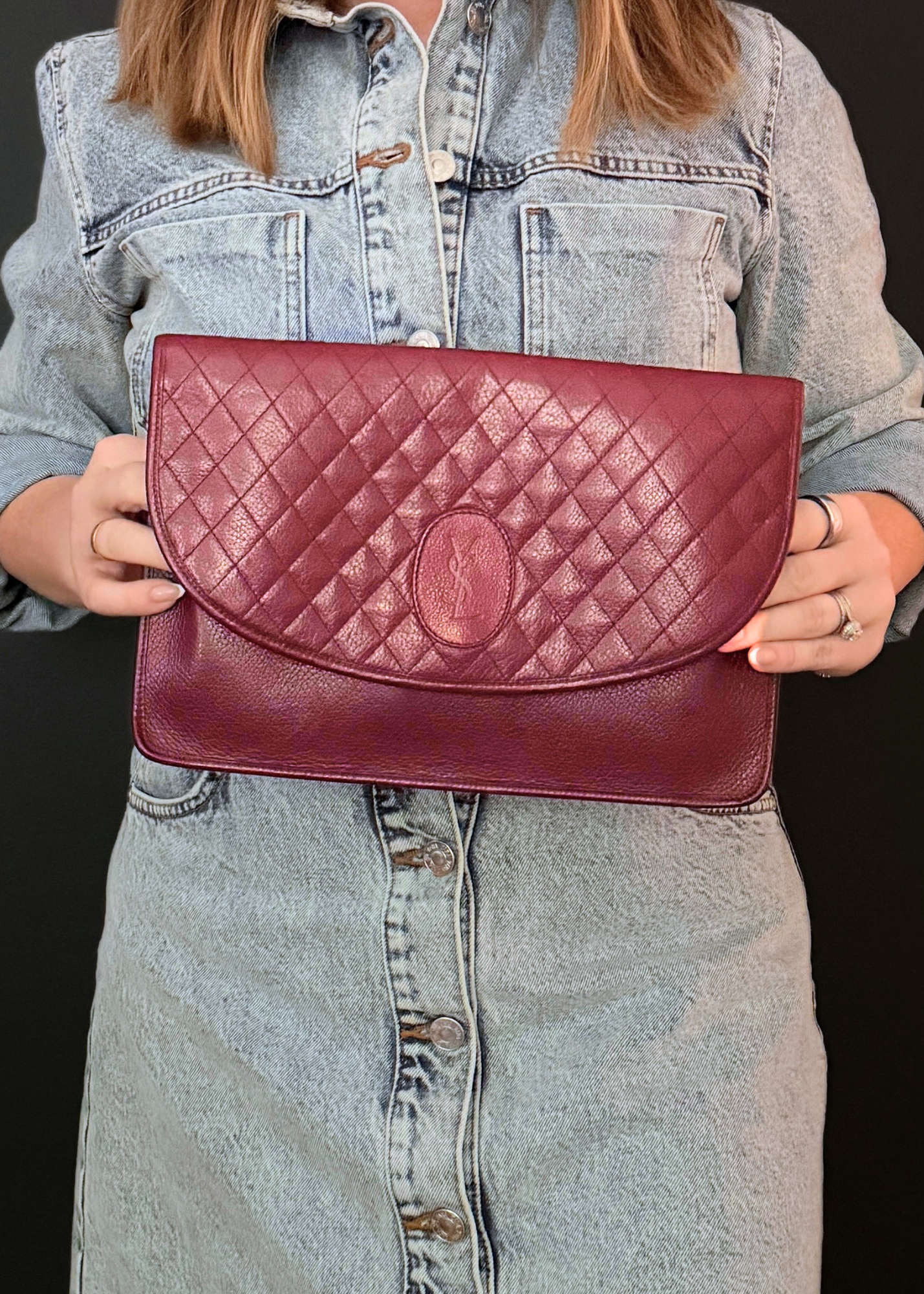 Person holding a burgundy red YSL quilted handbag against a black background