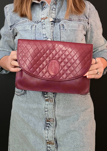Person holding a burgundy red YSL quilted handbag against a black background