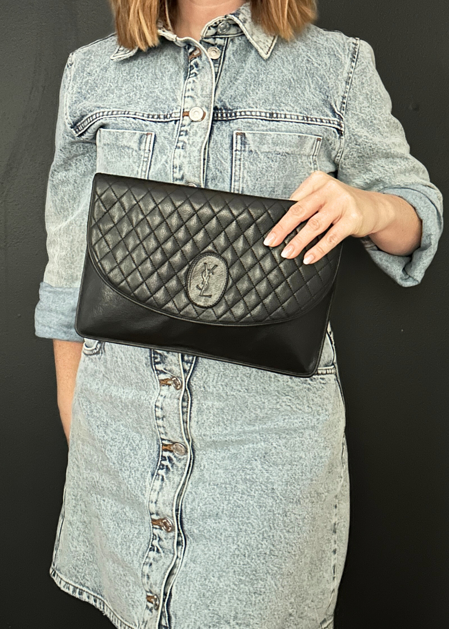 Person holding a black quilted YSL clutch bag against a dark background