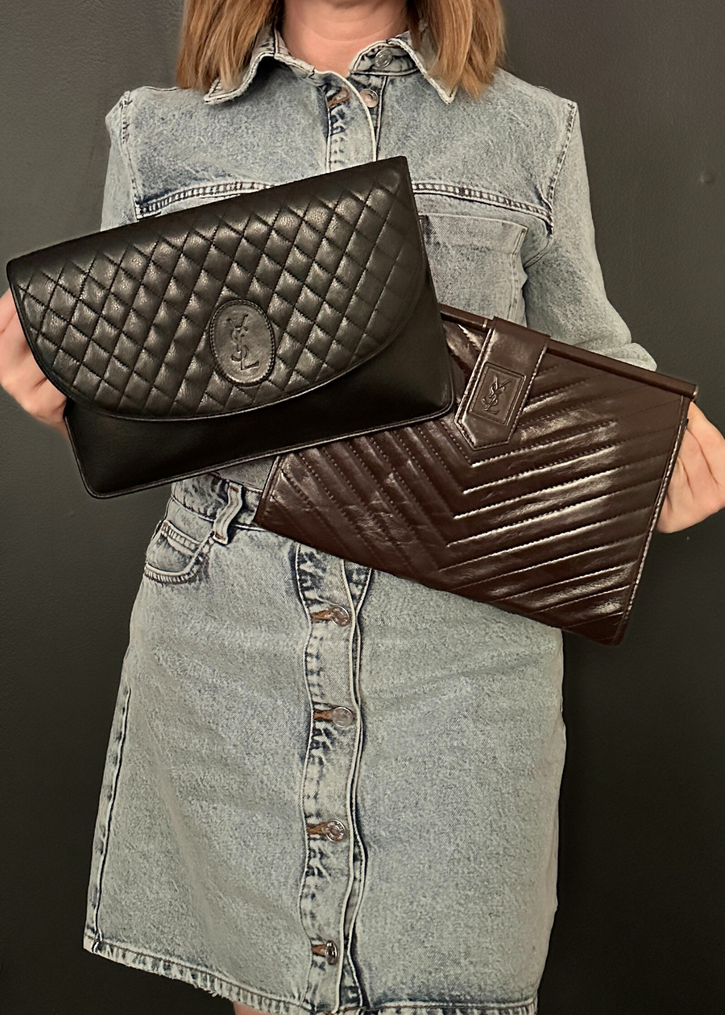 Person holding two vintage YSL clutch bags, one black quilted and one brown, against a dark background.
