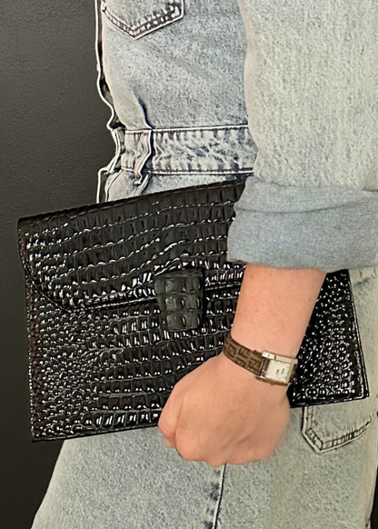 Person holding a black textured YSL clutch bag with a watch on wrist