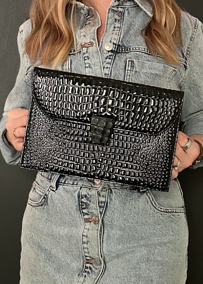Person holding a black textured YSL clutch against a neutral background