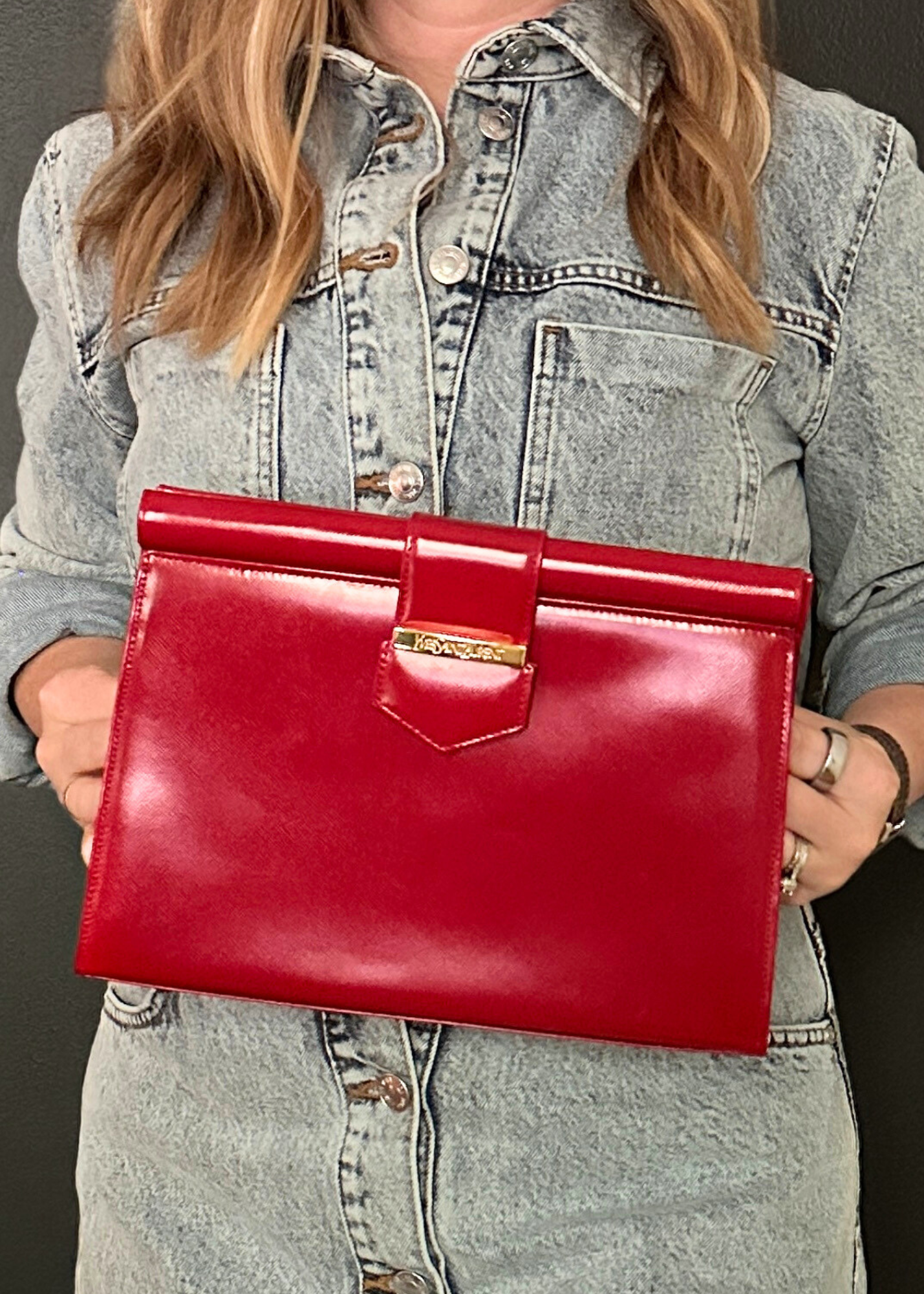 Person holding a YSL red clutch bag against a dark background